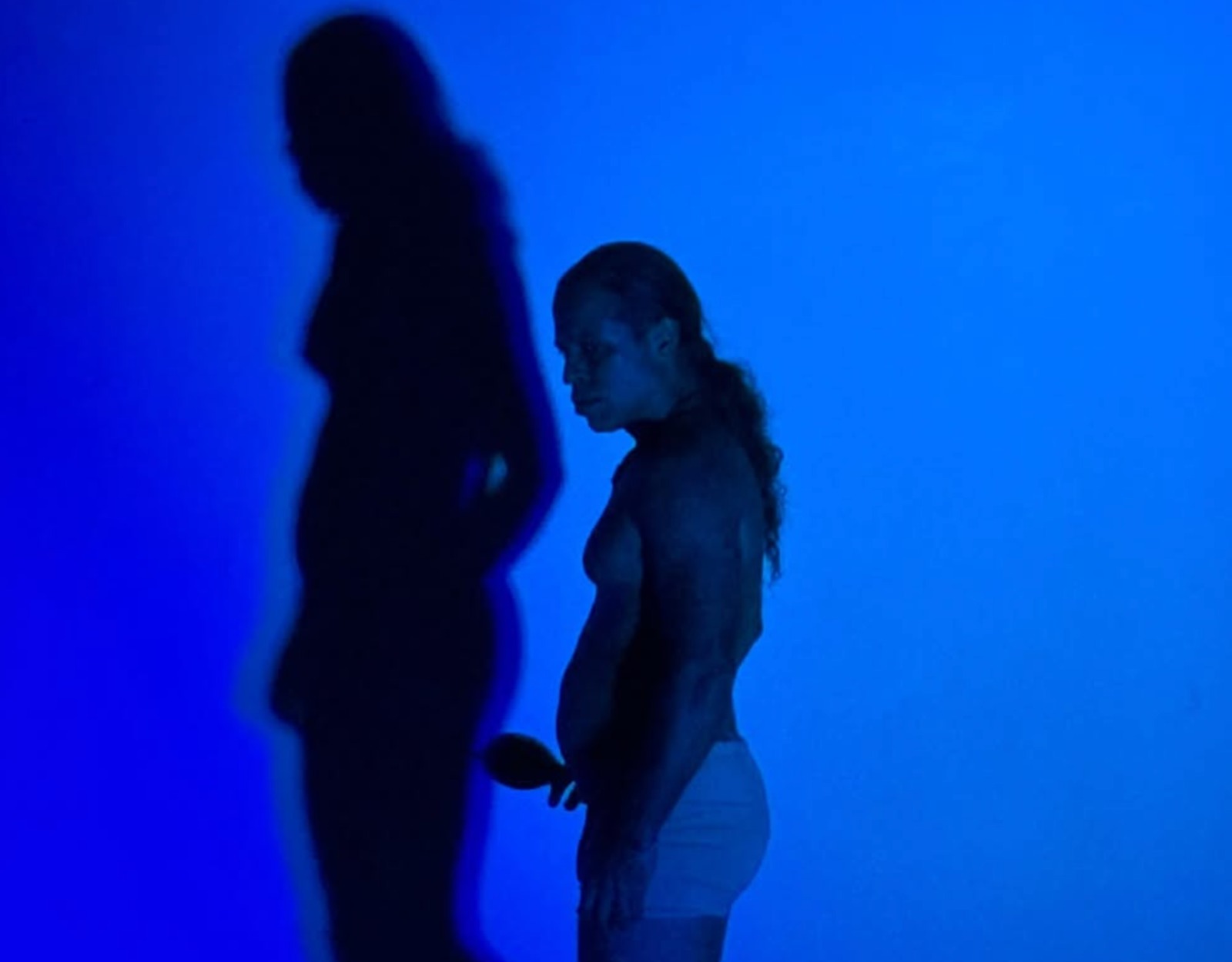 Performer de perfil diante de sua sombra ampliada em luz azul