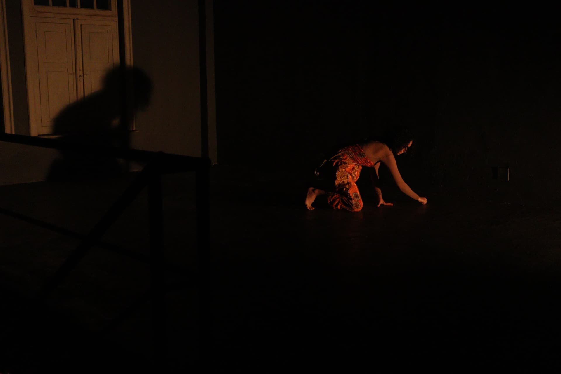 Atriz recolhida ao chão em foco de luz baixa