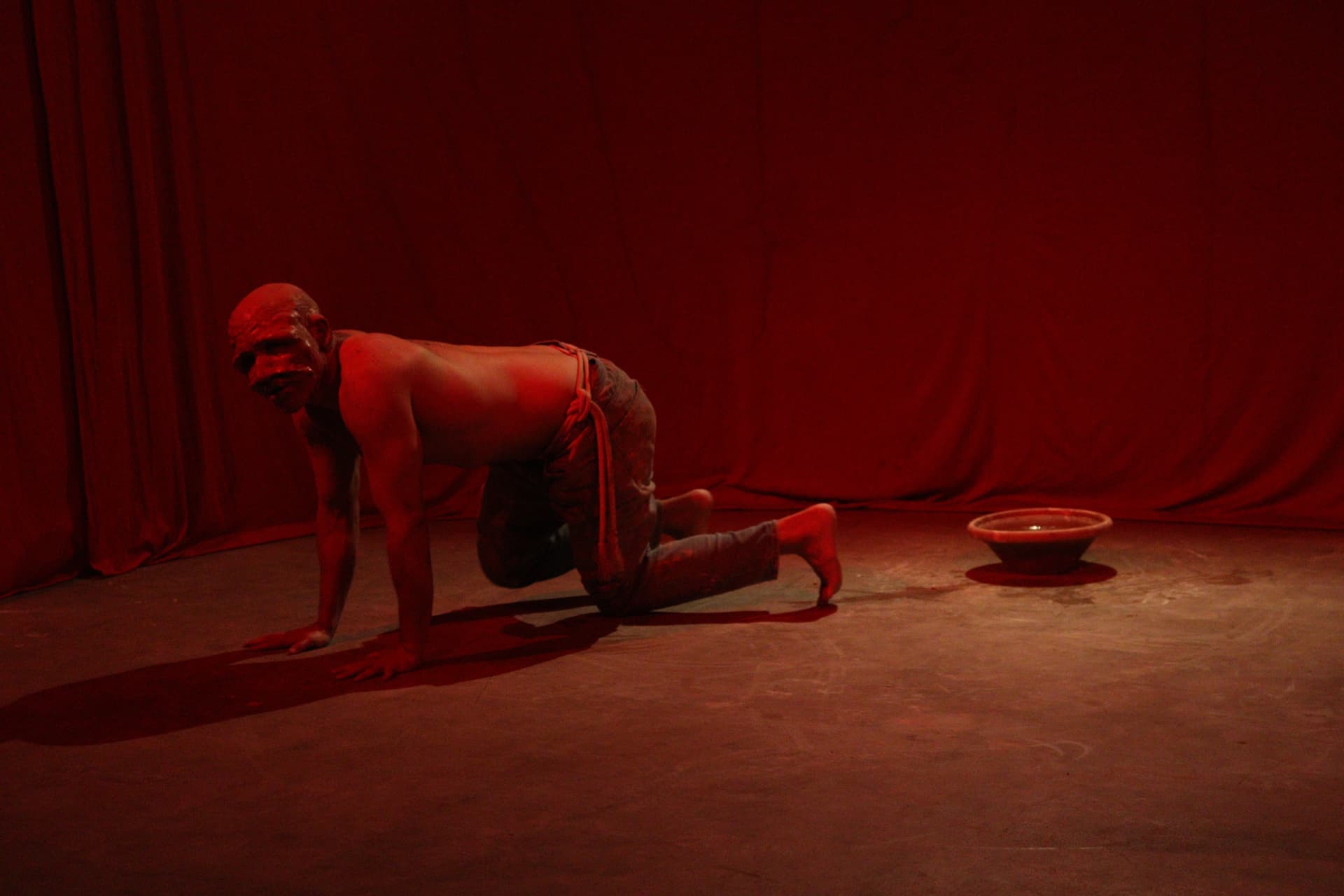 Performer engatinhando diante de cortina vermelha