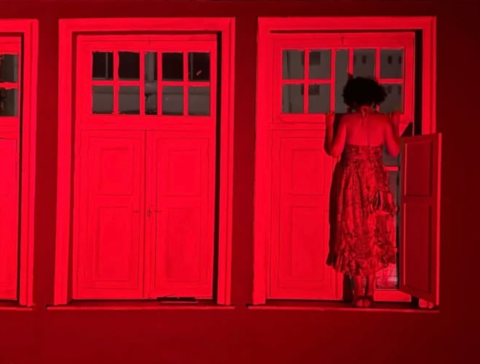 Performer de vestido na janela do casarão em luz vermelha