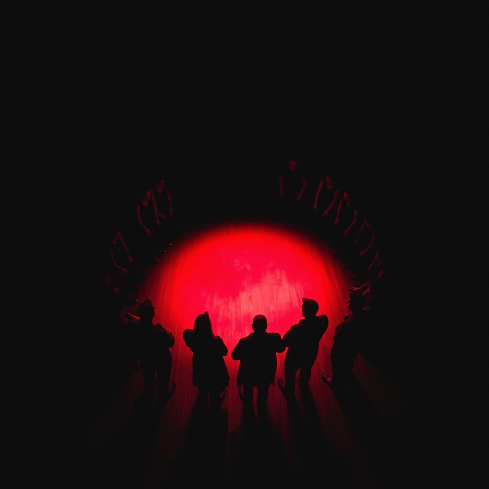 Grupo de atores em roda sobre círculo de luz vermelha